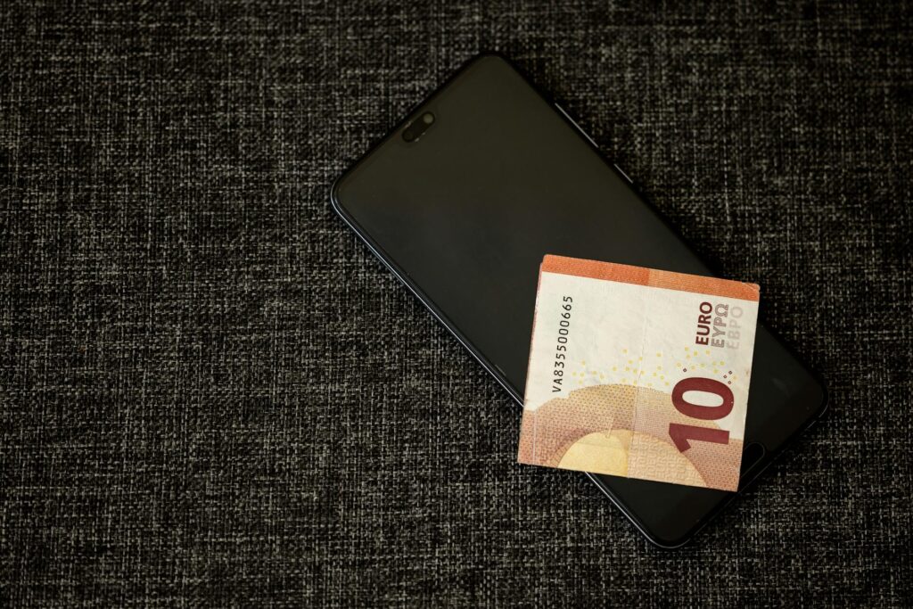 A 10 euro banknote placed on a smartphone on a textured dark fabric background. (Photo by Engin Akyurt on Pexels)