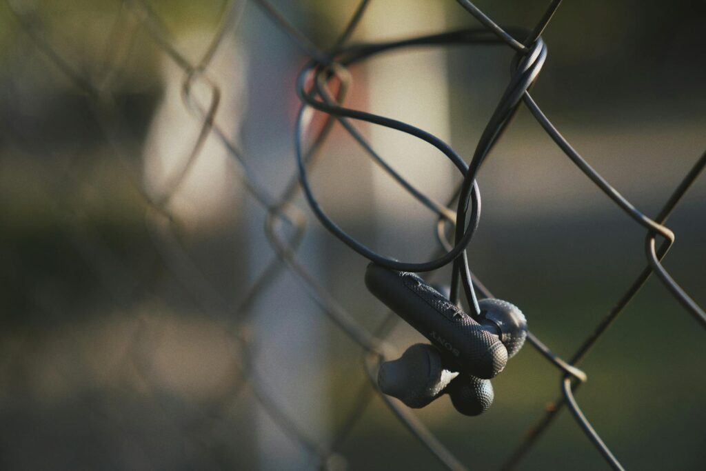 Close-up of wireless earbuds hanging on a wire fence in soft outdoor lighting, showcasing modern ... (Photo by Olena Bohovyk on Pexels)