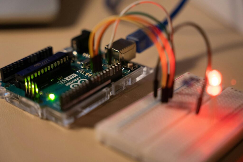 Close-up of Arduino microcontroller connected to a breadboard with a glowing LED. (Photo by Chengxin Zhao on Pexels)