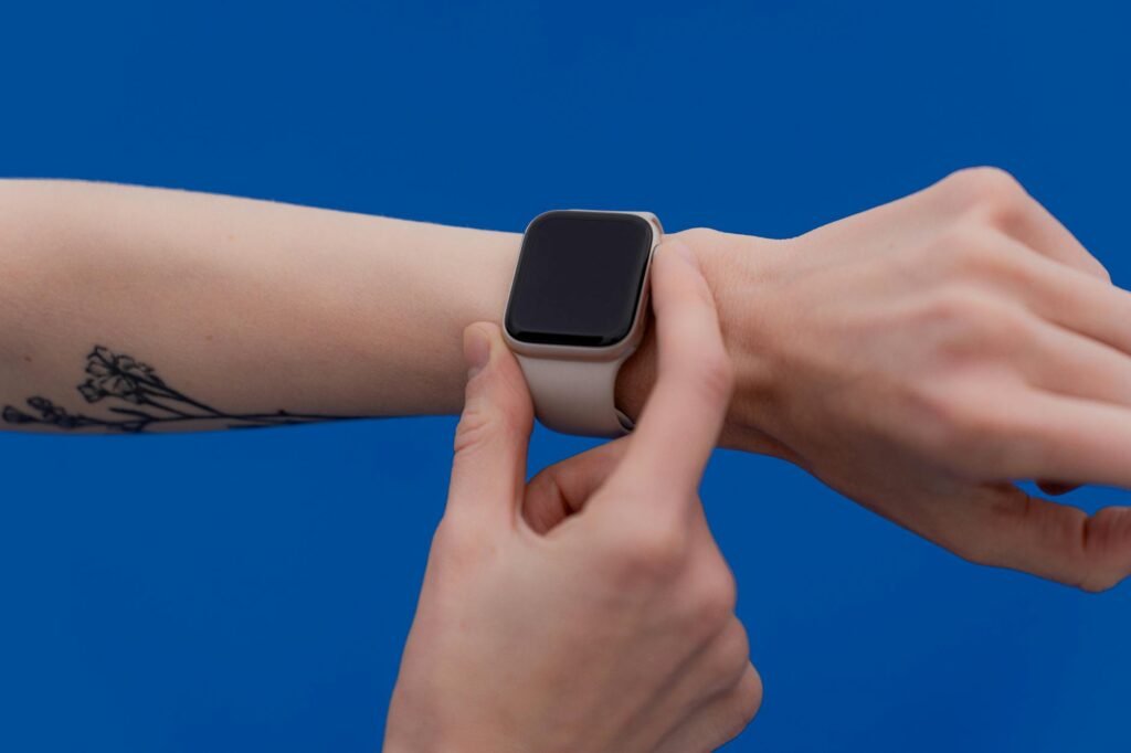 A person adjusting a modern smart watch against a bright blue background. (Photo by Anastasiya Badun on Pexels)