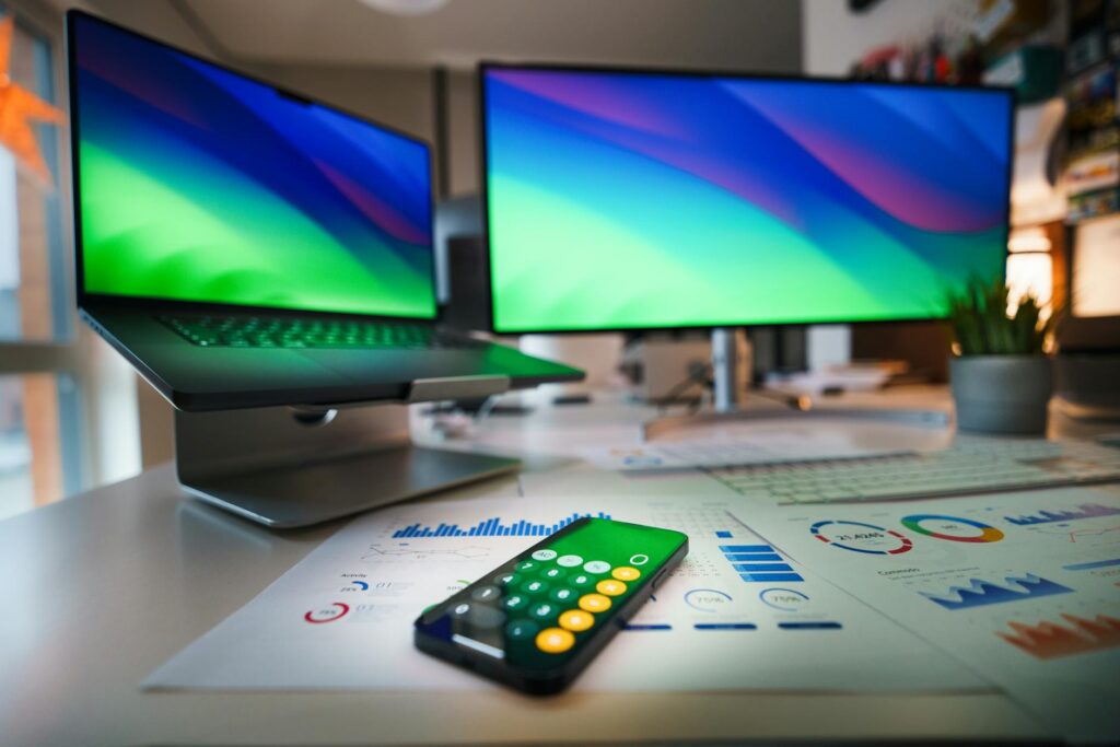 Contemporary office desk featuring a laptop, smartphone calculator app, and business graphs. (Photo by Jakub Zerdzicki on Pexels)