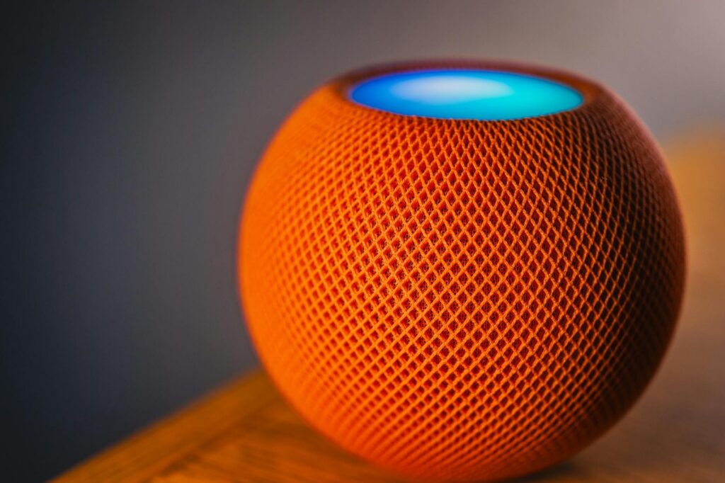 Close-up of an orange smart speaker with a glowing blue light, showcasing modern technology. (Photo by Robert So on Pexels)