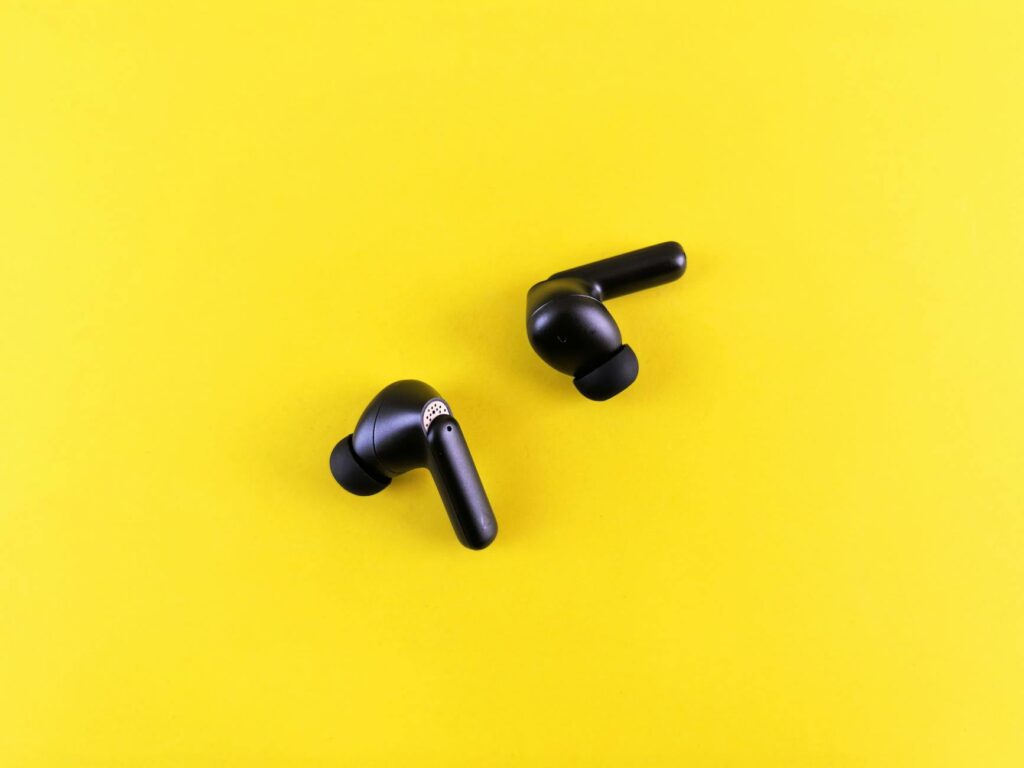 Minimalist black wireless earbuds on a bright yellow backdrop for tech and lifestyle themes. (Photo by Andrey Matveev on Pexels)