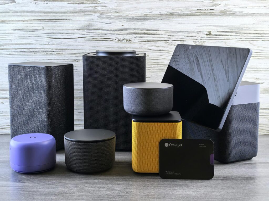 A collection of various smart home speakers and tablet displayed on a wooden surface. (Photo by Andrey Matveev on Pexels)