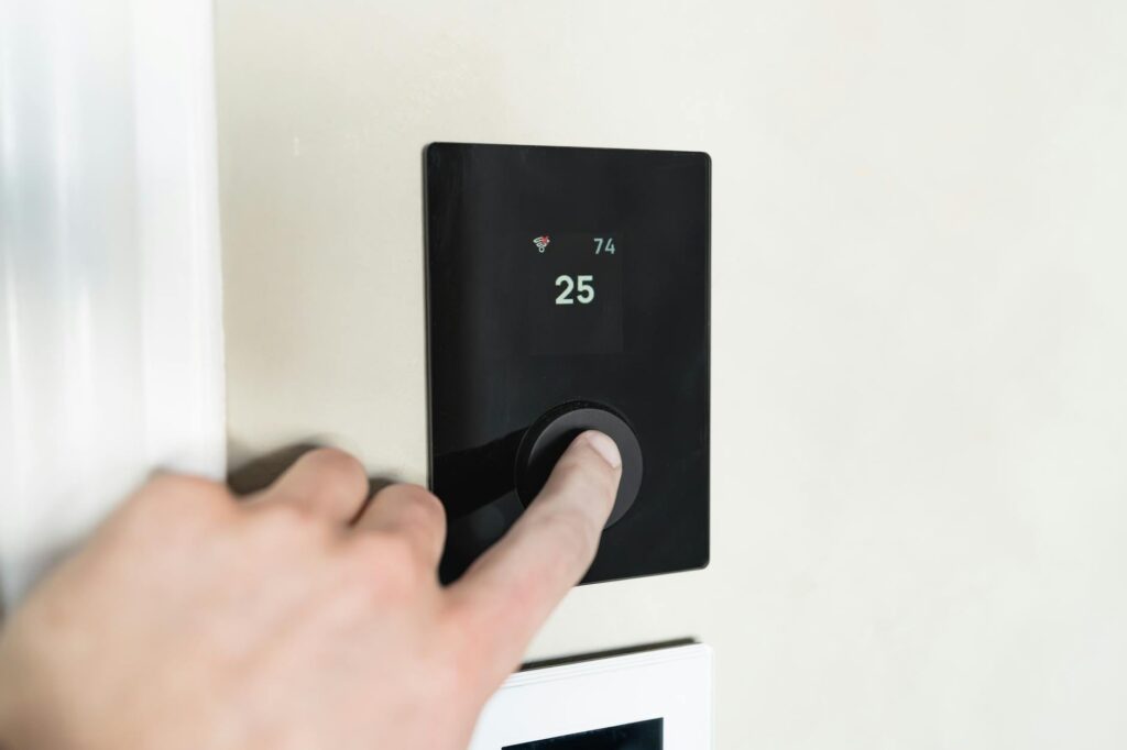 Close-up of a hand adjusting a sleek, modern smart thermostat on a wall. (Photo by HUUM  │sauna heaters on Pexels)