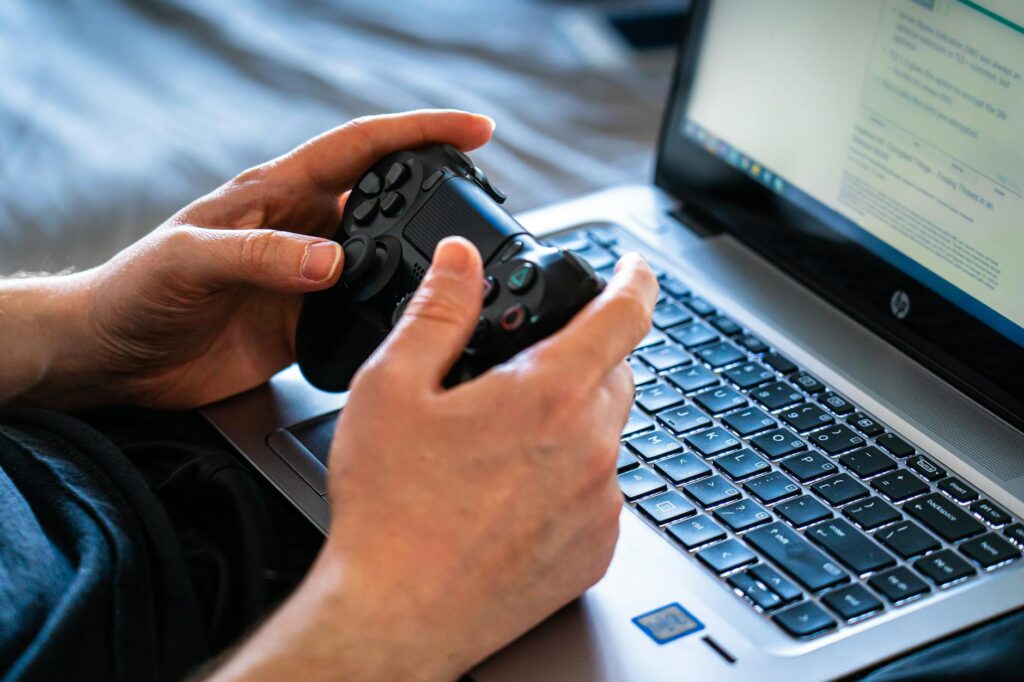 Person holds a gaming controller while interacting with a laptop, emphasizing modern gaming techn... (Photo by Castorly Stock on Pexels)
