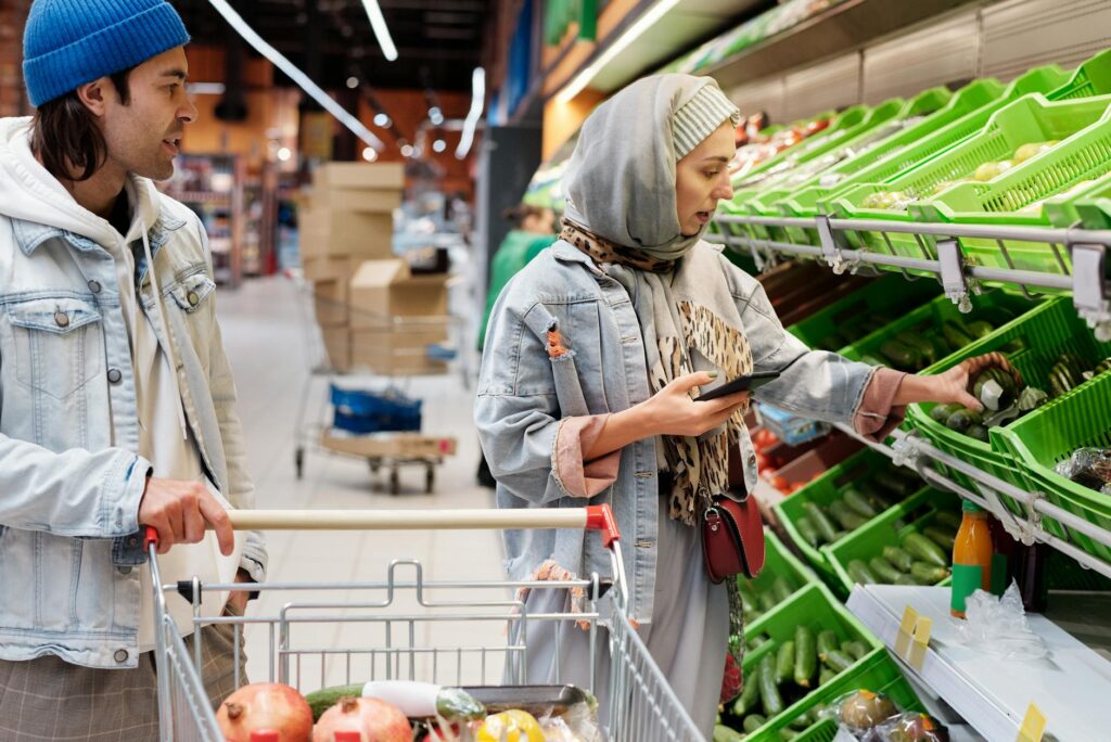 Diverse couple shopping for vegetables in a supermarket, discussing choices with smartphone. (Photo by Jack Sparrow on Pexels)
