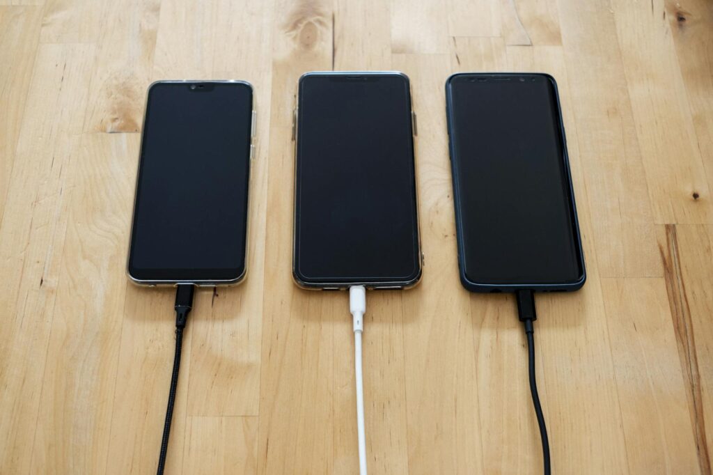 Three smartphones connected to chargers on a wooden surface, showcasing modern technology (Photo by Stanley Ng on Pexels)
