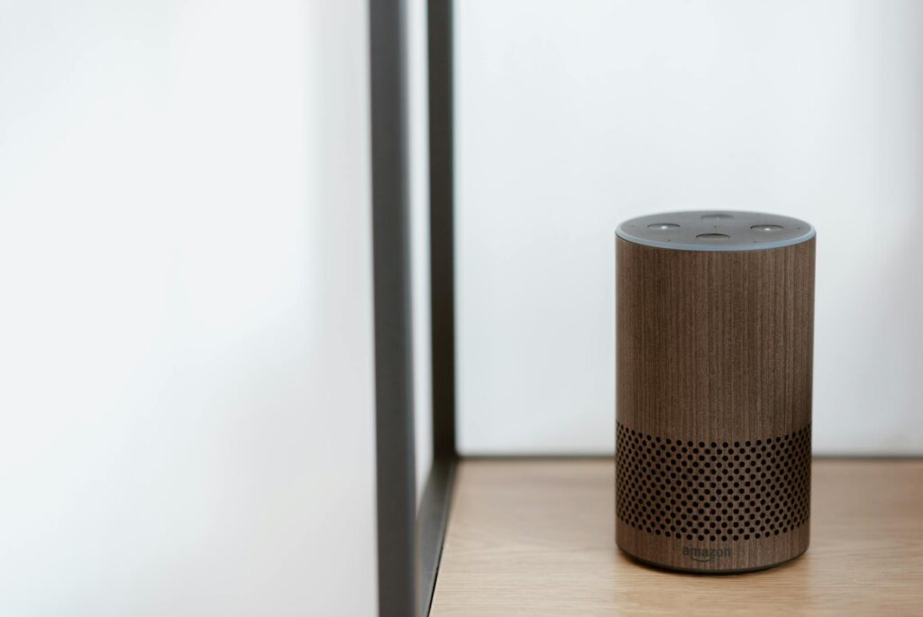 A sleek, modern smart speaker displayed on a wooden shelf in a minimalist room setting. (Photo by Anete Lusina on Pexels)