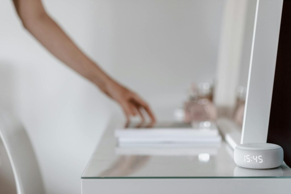 A smart speaker with a digital clock display placed on a minimalist desk setting, hand in backgro... (Photo by Anete Lusina on Pexels)