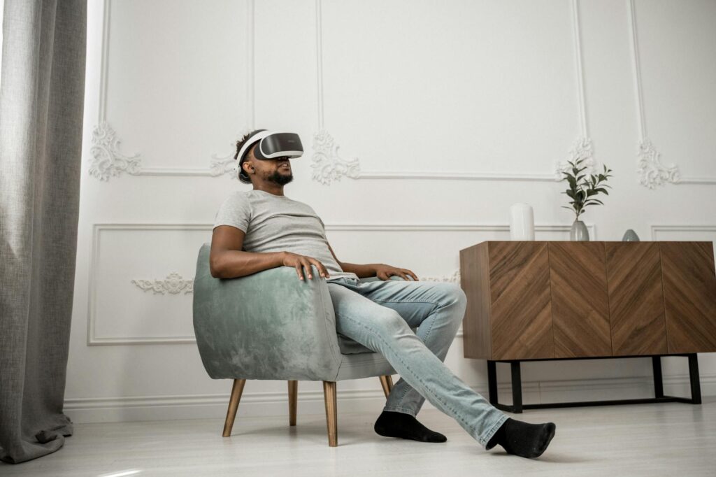 Adult man sitting in a stylish room, wearing a VR headset, showcasing modern technology and relax... (Photo by Tima Miroshnichenko on Pexels)