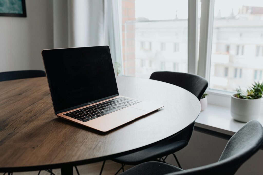 A cozy workspace with a laptop on a wooden table by a window offering natural light. (Photo by www.kaboompics.com on Pexels)