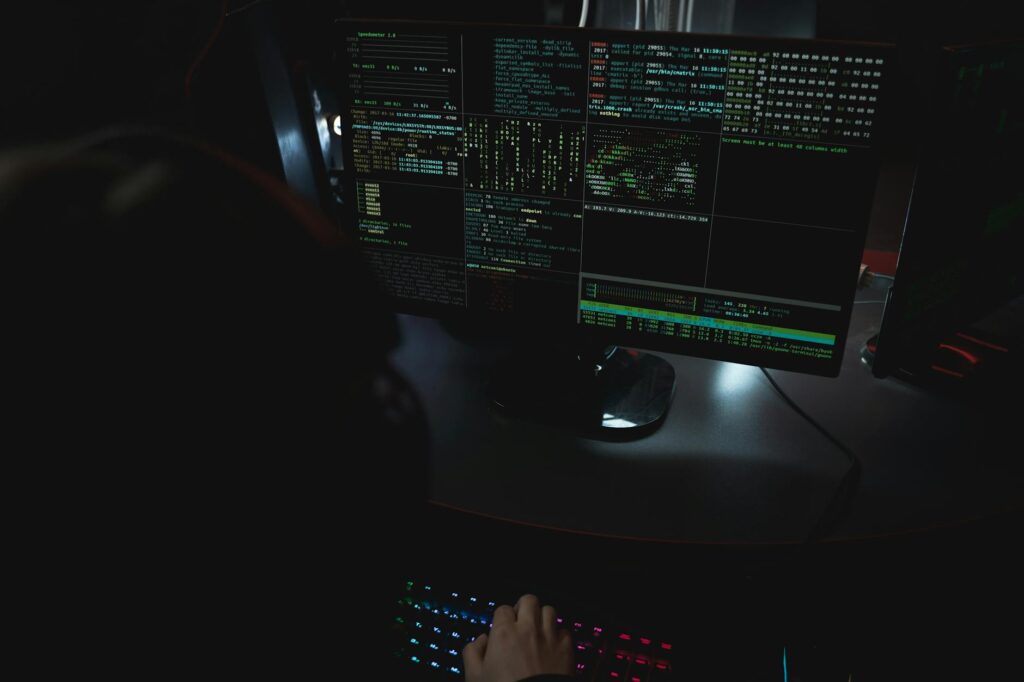 Dark room setup with code displayed on PC monitors highlighting cybersecurity themes. (Photo by Tima Miroshnichenko on Pexels)