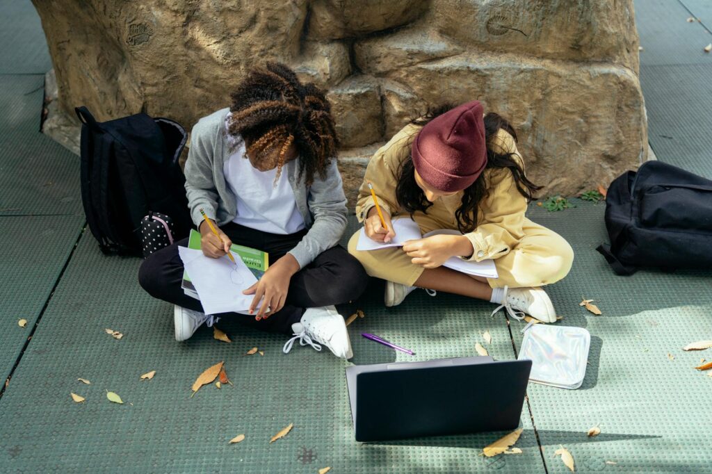 From above of anonymous diverse schoolkids taking notes in copybook and drawing on paper while st... (Photo by Mary Taylor on Pexels)