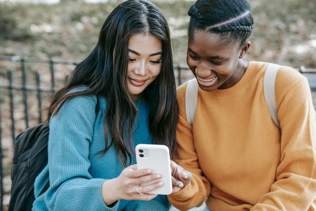 Young happy divers female friends in casual wear and backpacks watching photos on mobile phone in... (Photo by Charlotte May on Pexels)