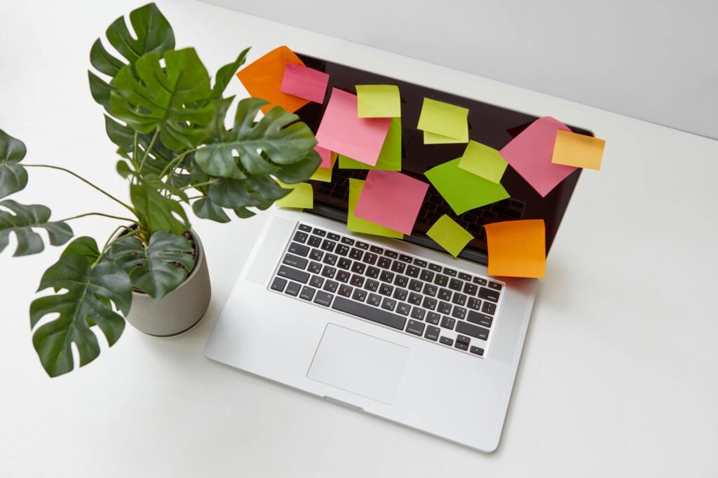 Top view of a desk featuring a laptop covered with sticky notes and a potted plant for productivi... (Photo by DS stories on Pexels)