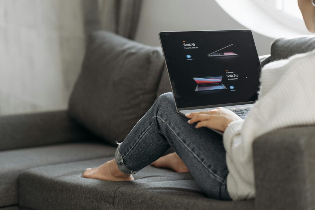 Woman sitting on a couch browsing laptops online. Perfect for online shopping or lifestyle contexts. (Photo by Pavel Danilyuk on Pexels)