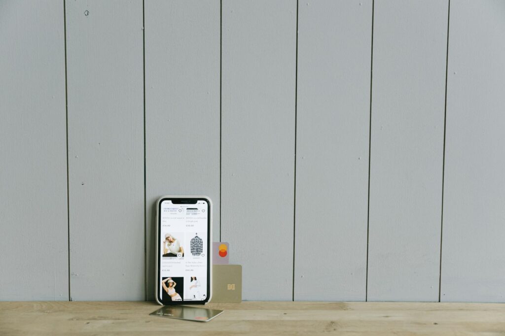 A smartphone displaying an ecommerce site with a credit card, set on a wooden surface, depicting ... (Photo by Ivan S on Pexels)