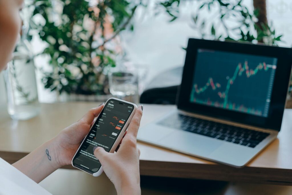 Businesswoman reviewing financial data on smartphone alongside laptop displaying graphs in modern... (Photo by Mikhail Nilov on Pexels)