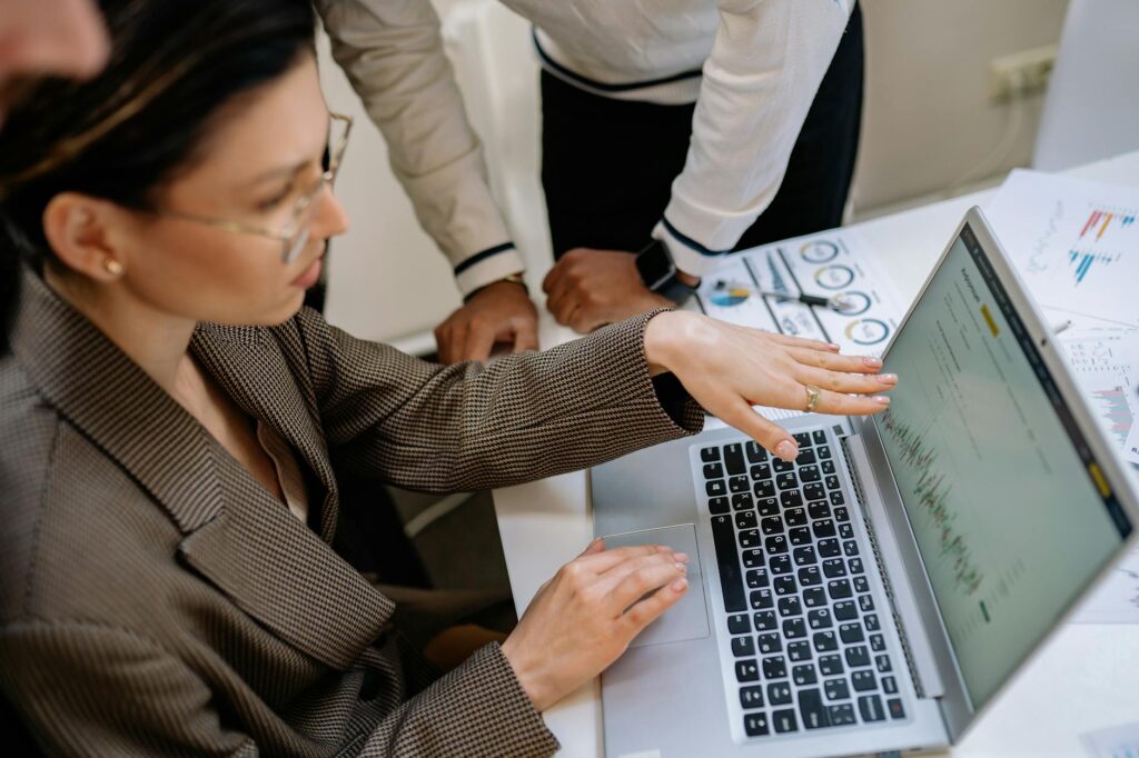 Two professionals focused on analyzing data charts on a laptop in an office setting. (Photo by Yan Krukau on Pexels)