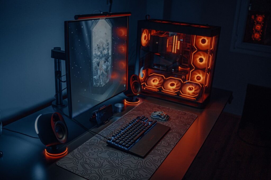 Sleek gaming desk setup featuring RGB lighting, large monitor, and gaming PC with glowing fans. (Photo by Atahan Demir on Pexels)