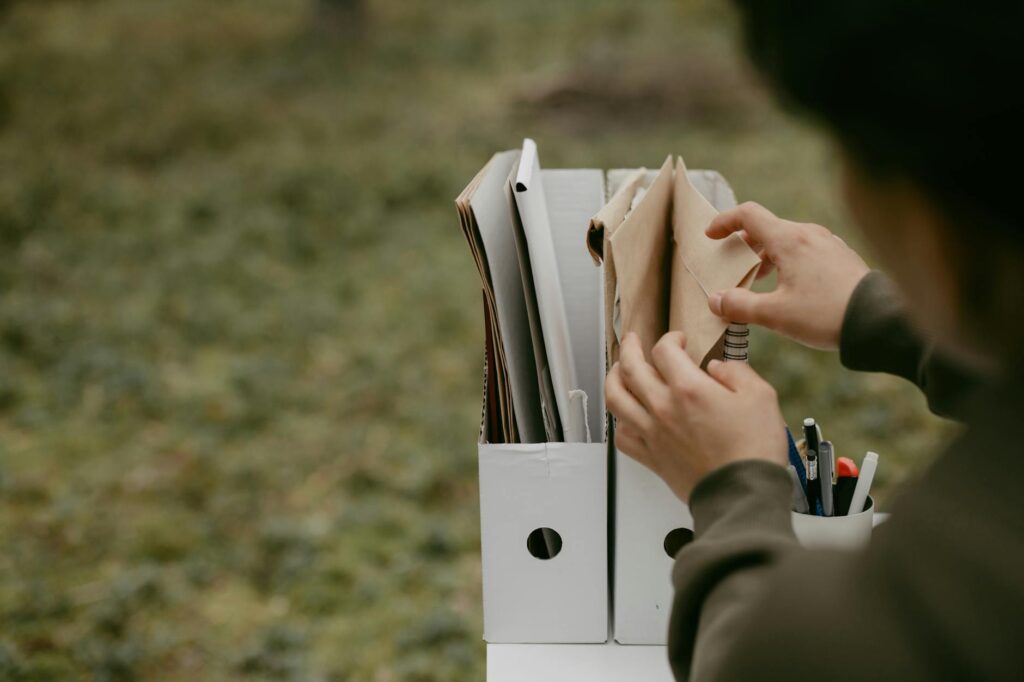 Person sorting documents in folders outdoors, hands visible, neutral tone. (Photo by cottonbro studio on Pexels)