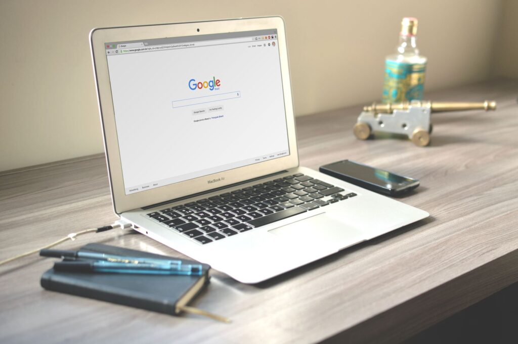 A neat workspace featuring a laptop displaying Google search, a smartphone, and a notebook on a w... (Photo by Caio on Pexels)